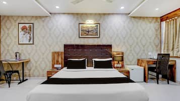 Una habitación de hotel con una cama grande, un escritorio, una silla, una mesita y un ventilador de techo.