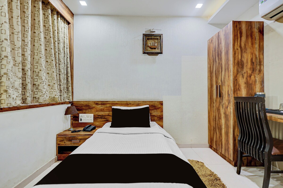 A bedroom with a wooden headboard, a bed with white bedding, a nightstand with a lamp, a desk, and a wardrobe.