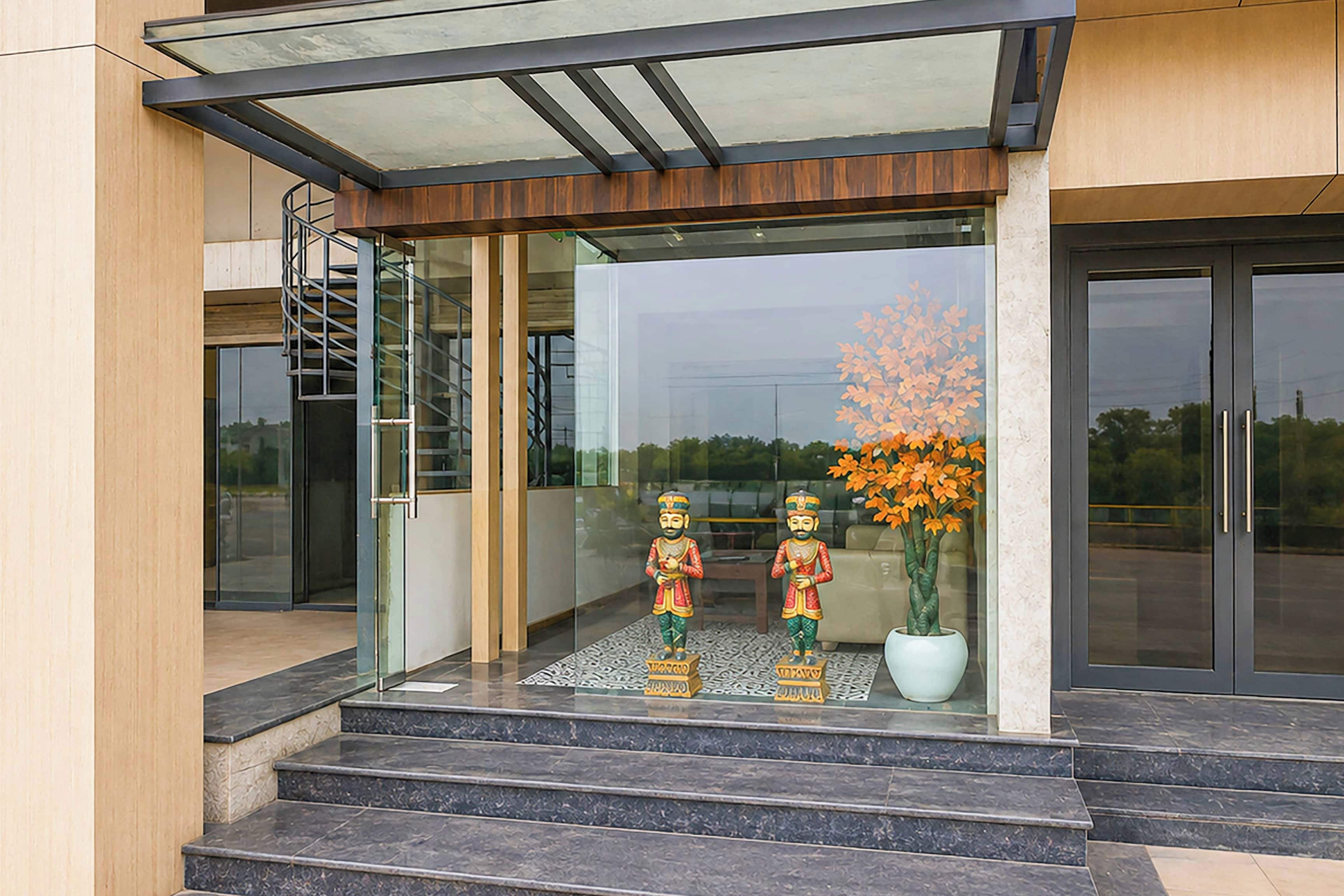 A modern building entrance with a glass door, a metal staircase, and two statues on the steps.