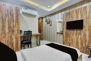 A hotel room with a bed, a desk, a chair, an air conditioning unit, a television, and a wall-mounted shelf.