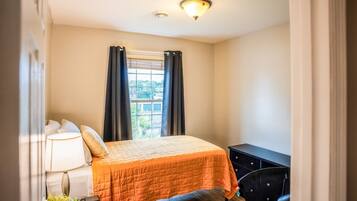 A bedroom with a bed, a desk, a lamp, and a window with curtains.