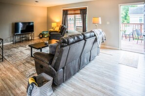 A living room with a leather sofa, a television, a coffee table, and a window with curtains.