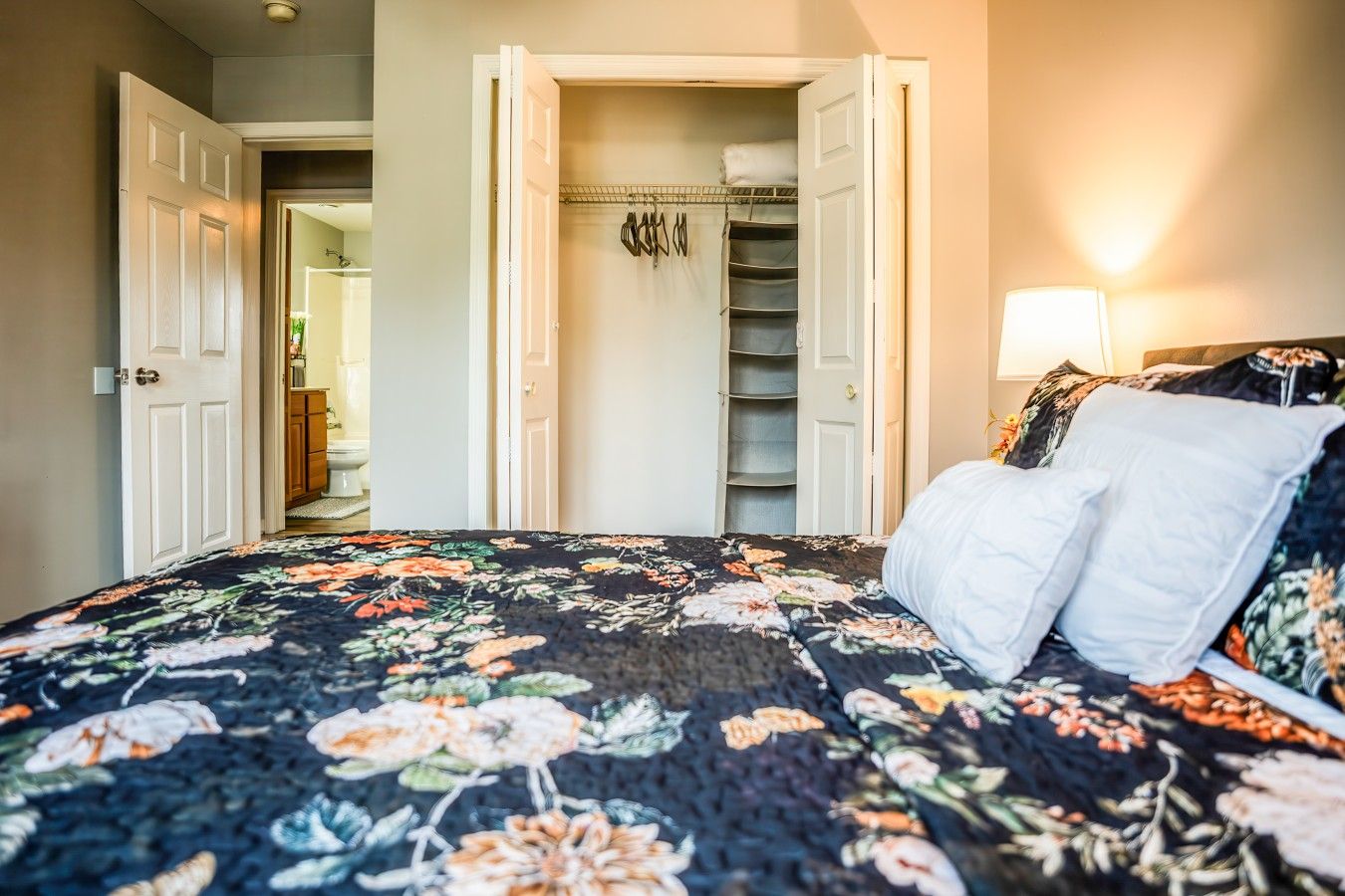 Une chambre à coucher avec un lit, une armoire où sont rangés des vêtements suspendus, et une porte qui donne sur une autre pièce.