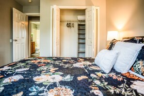 A bedroom with a bed, a closet with hanging items, and a door leading to another room.