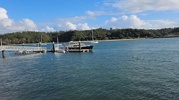 Ein Küstenhafen mit vertäuten Booten, einer Pier und einem bewaldeten Hügel im Hintergrund.