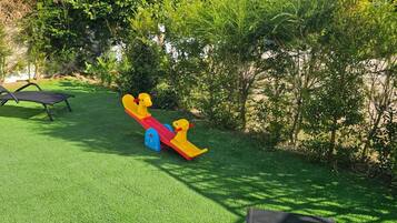 A playground with a seesaw and a black lounge chair on artificial grass.