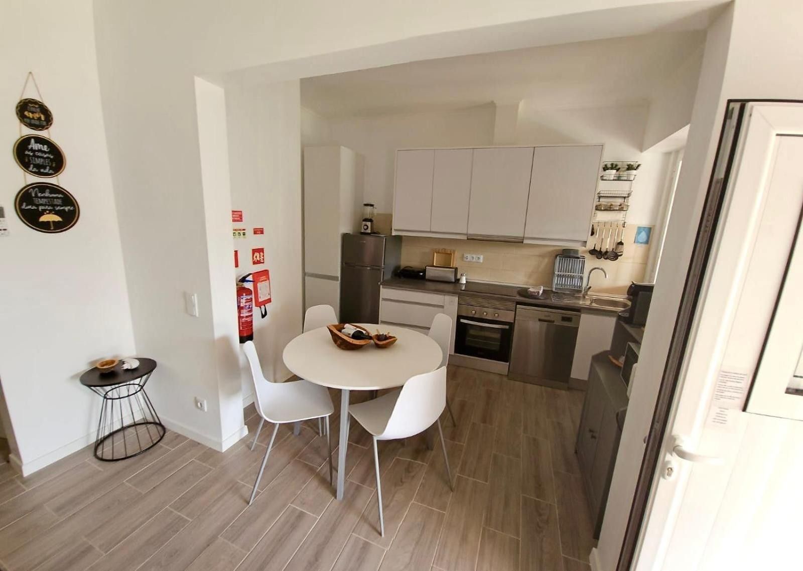 Une cuisine compacte avec des meubles blancs, un réfrigérateur, une cuisinière et un évier. On y trouve également un petit coin repas avec une table ronde et deux chaises.