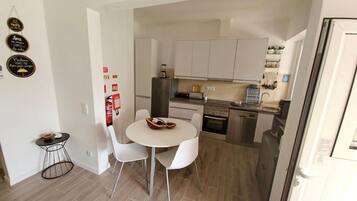 Une cuisine compacte avec des meubles blancs, un réfrigérateur, une cuisinière et un évier. On y trouve également un petit coin repas avec une table ronde et deux chaises.