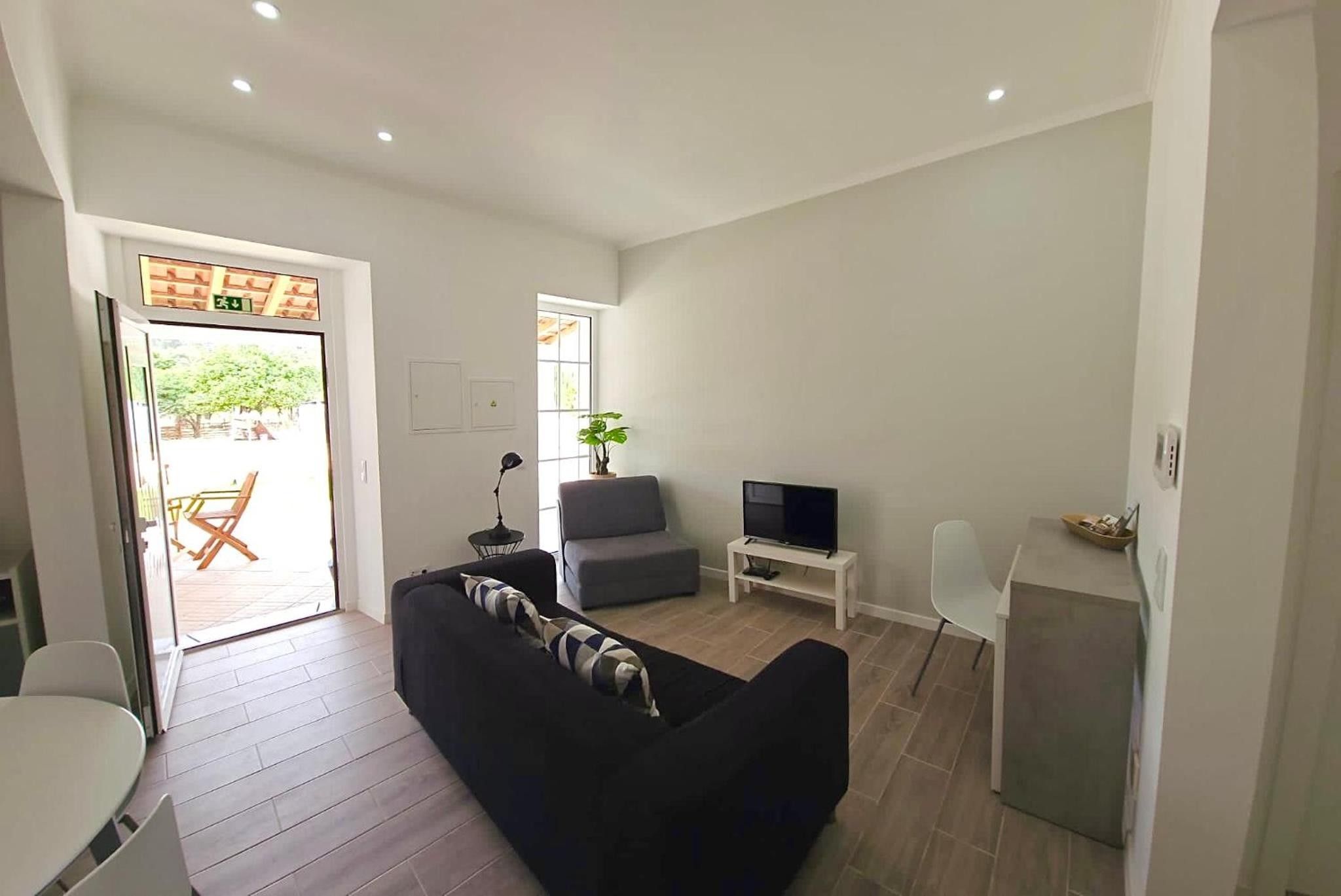 A modern living room with a black sofa, a grey armchair, a TV, and a small white table.