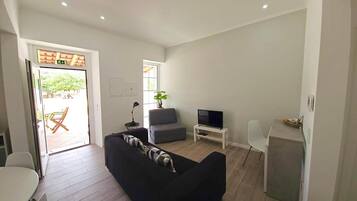 A modern living room with a black sofa, a grey armchair, a TV, and a small white table.