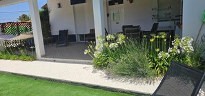 A covered outdoor seating area with a patio table and chairs, a small garden with white flowers, and a door marked with the number 10.