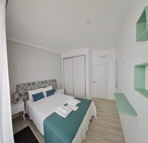 A bedroom with a bed, nightstands, a wardrobe, and a green shelf unit.