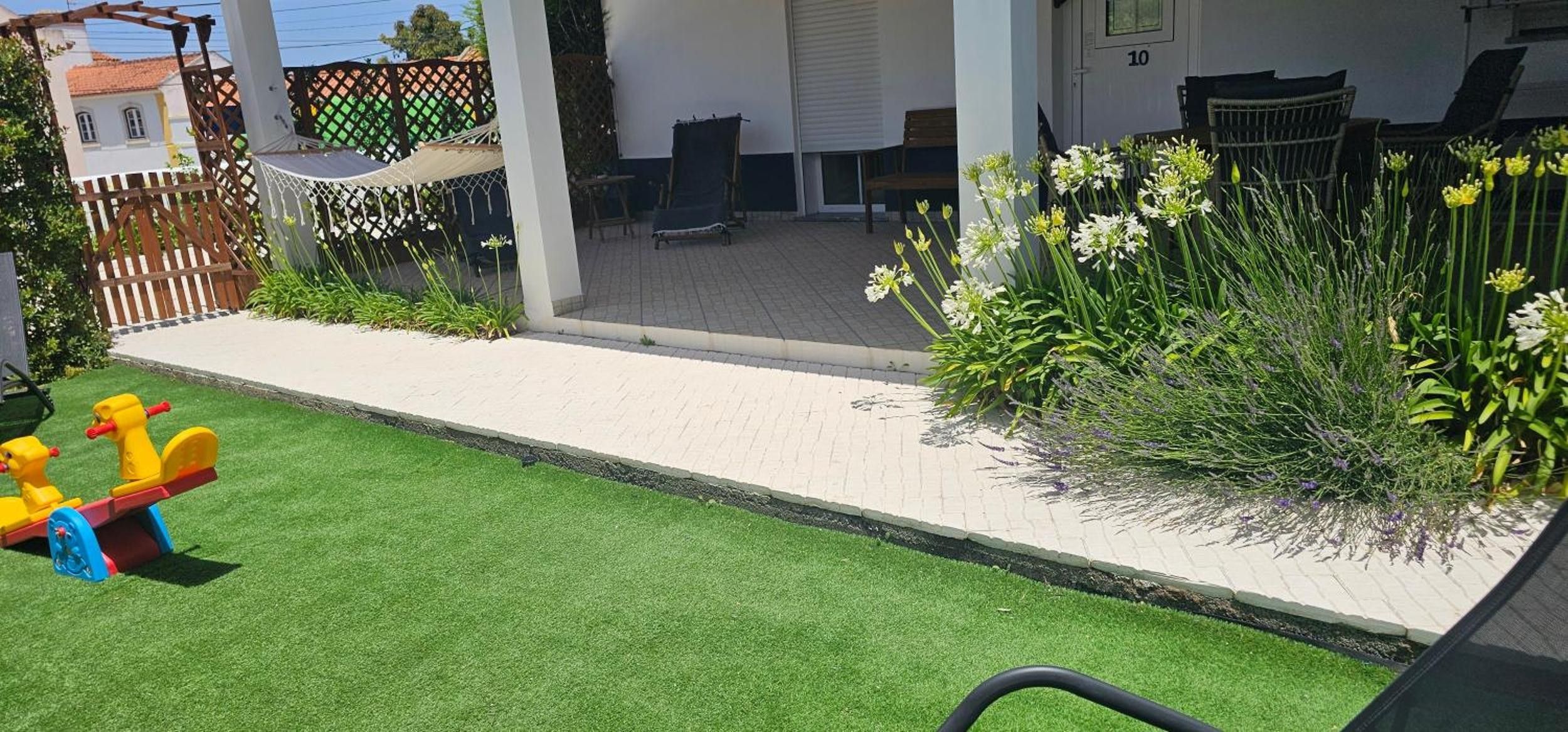 A patio area with artificial grass, a children's play structure, and a variety of plants.