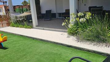 A patio area with artificial grass, a children's play structure, and a variety of plants.