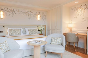 Habitación de hotel con cama, dos sillones, una mesita redonda, escritorio y lámpara.