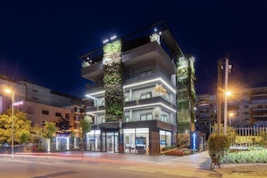 A modern multi-story hotel with a glass facade, outdoor seating area, and vertical gardens. - Moncafe Hotel Boutique Spa (Tirana)