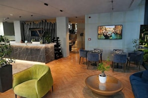 A hotel reception area with a reception desk, seating area, and a television displaying a cityscape. - Moncafe Hotel Boutique Spa (Tirana)
