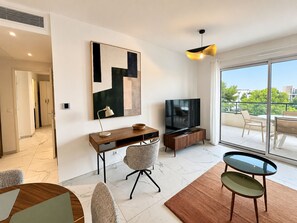 A modern living room with a flat-screen TV, a desk, and a chair. There is a large window with a view of the outdoors. - Solemare 402 by Avecoeur (Villeneuve-Loubet)