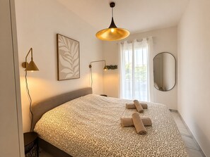 Een slaapkamer met een bed, een bedlamp, een spiegel aan de muur en een raam met gordijnen.