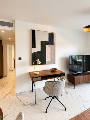 Een moderne woonkamer met een houten bureau, een comfortabele fauteuil, een flatscreen televisie en een eigentijds abstract schilderij.