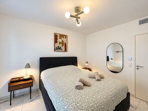 A bedroom with a bed, a nightstand, a lamp, a wall-mounted mirror, and a ceiling light fixture. - Solemare 402 by Avecoeur (Villeneuve-Loubet)