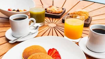 A breakfast setting with pancakes, fruit, and beverages on a wooden table by a pool.