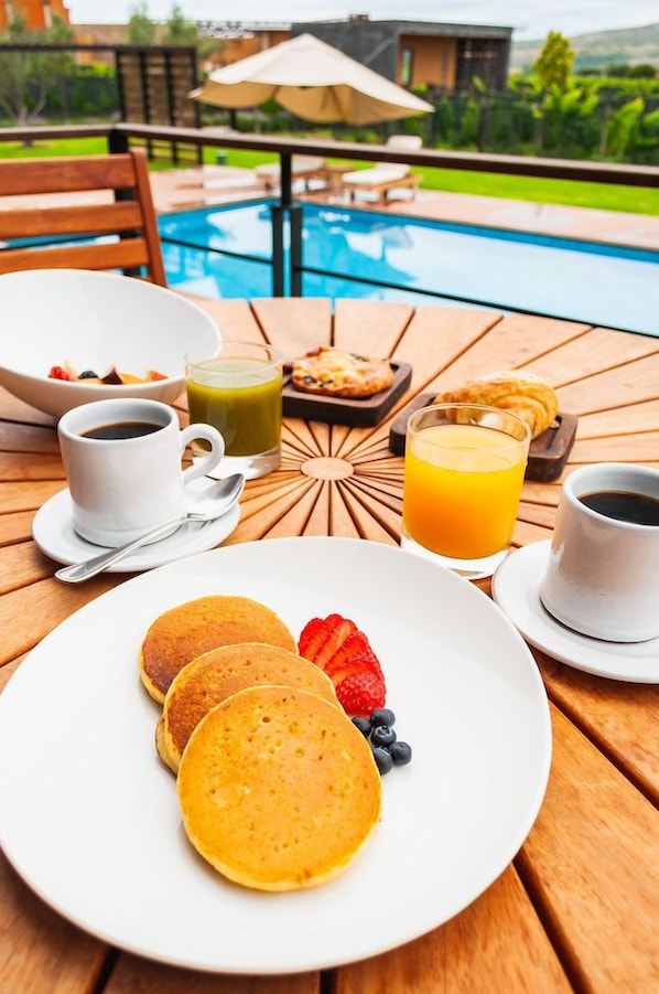A breakfast setting with pancakes, fruit, and beverages on a wooden table by a pool. - Hotel Tres Raices (Dolores Hidalgo)