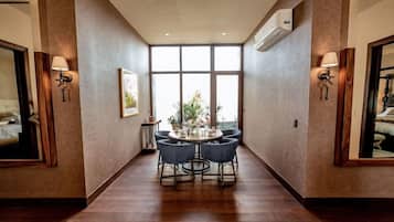 A hotel room with a large window, a round dining table with chairs, and two wall-mounted lamps.