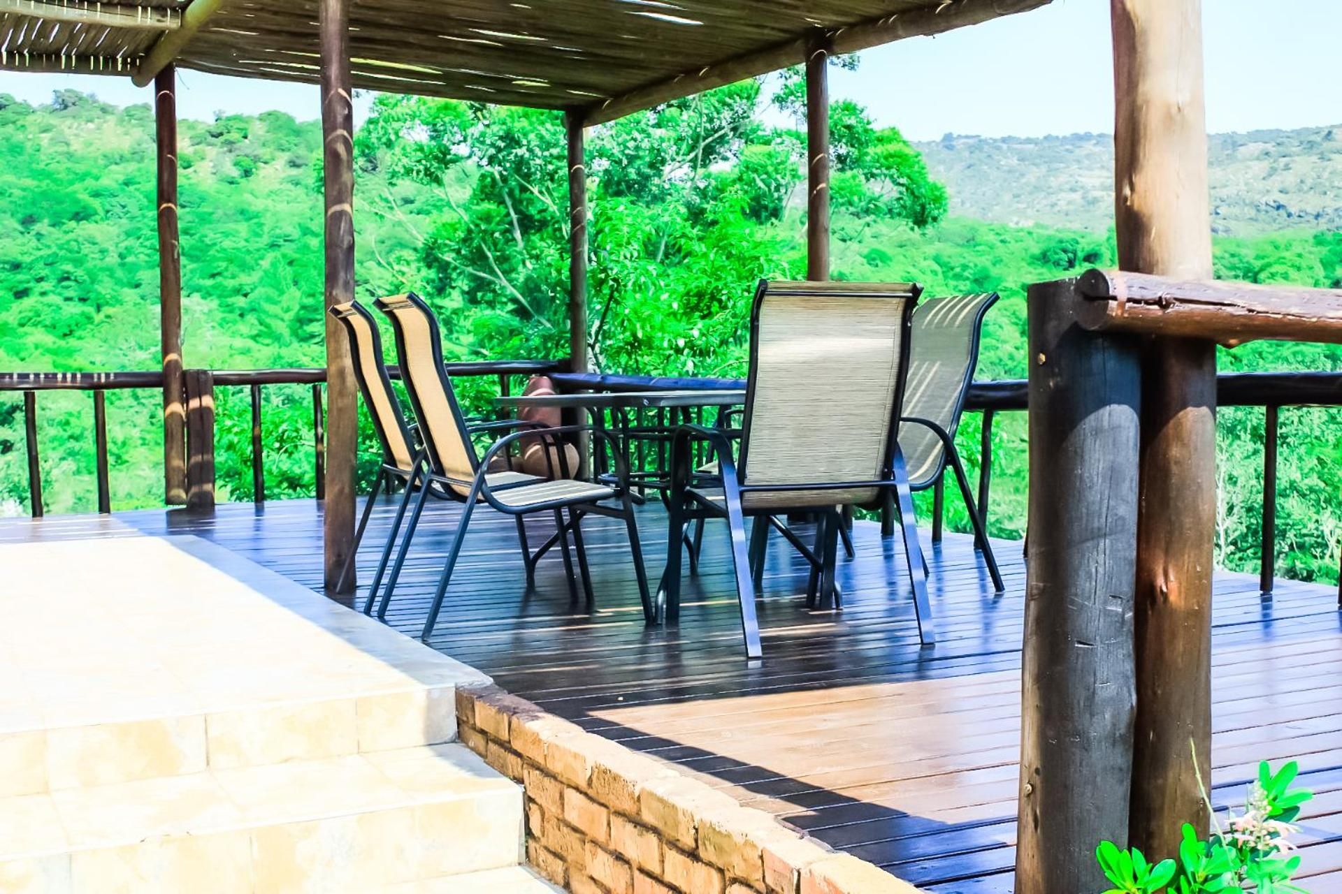 An outdoor deck with a table and chairs, surrounded by a wooden railing, overlooking a lush green landscape.