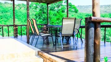 An outdoor deck with a table and chairs, surrounded by a wooden railing, overlooking a lush green landscape.