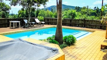 Una piscina rectangular con cubierta de madera, rodeada por una valla de madera, y vista a un paisaje montañoso.