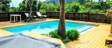 A rectangular swimming pool with a wooden deck, surrounded by a wooden fence, and a view of a mountainous landscape.