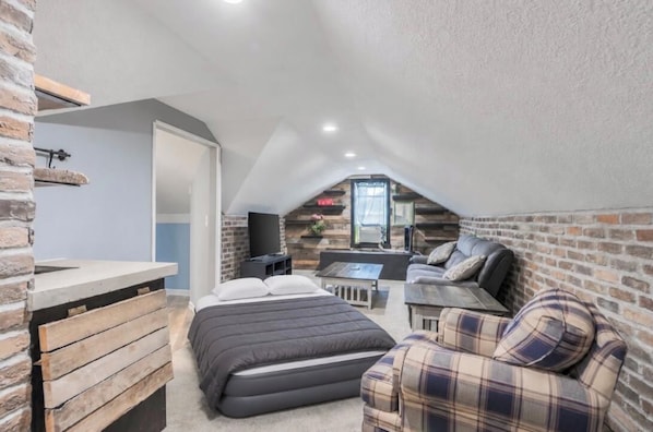 A compact room with a loft bed, a sofa, a small table, and a TV.