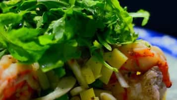 Ein Teller mit einem Meeresfrüchtegericht, möglicherweise Garnelen, belegt mit grünem Salat und gewürfelten Kartoffeln.