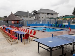 A swimming pool with a blue deck, a ping pong table, and rows of chairs. - WILLOW JOVIC SUITES (Bwari)