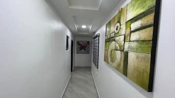 Um corredor com piso de azulejos, paredes brancas e uma grande pintura abstrata à direita.