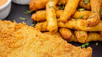 Um prato com salgados empanados e fritos, possivelmente incluindo tiras de frango, um filé de carne empanado e um molho para acompanhar.