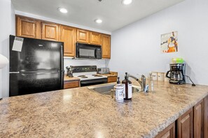 A kitchen with wooden cabinets, a black refrigerator, a microwave, a stove, a sink, and a coffee maker. - Apres Tahoe 4BR Mountain Home (Stateline)