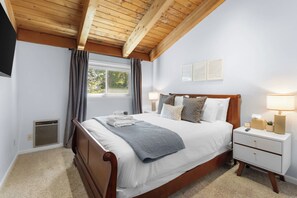 A bedroom with a wooden bed, bedside lamps, a window with curtains, and a small bedside table. - Apres Tahoe 4BR Mountain Home (Stateline)