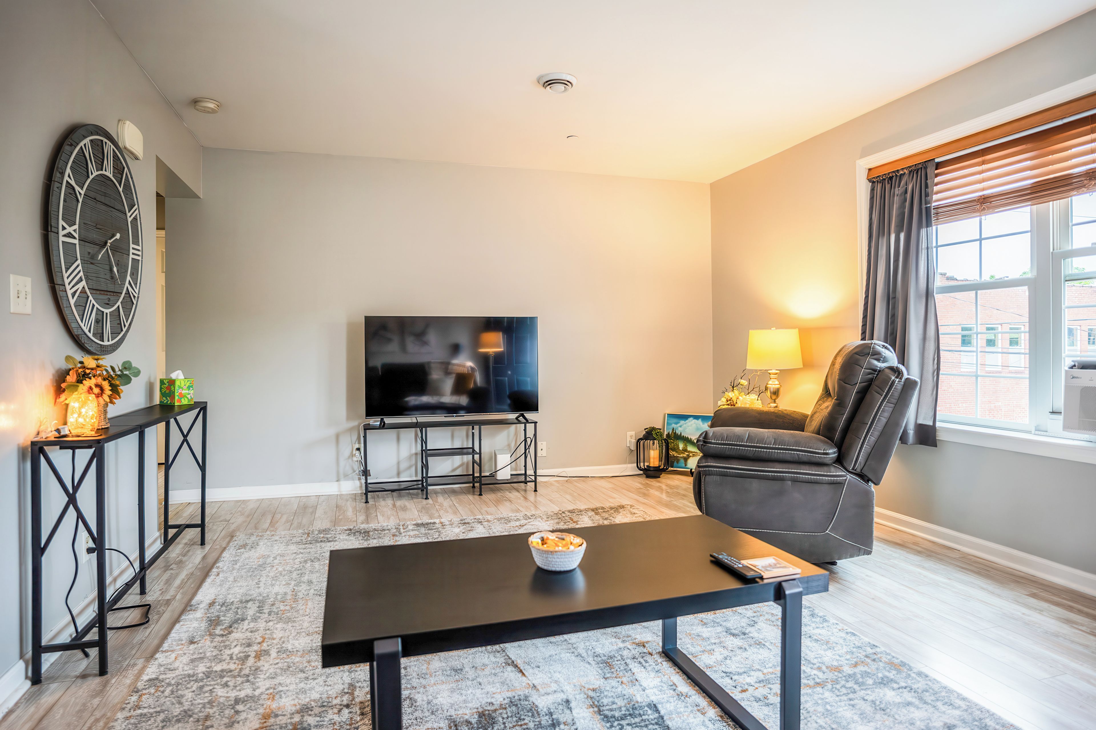 A living room with a flat-screen TV, a black leather sofa, a coffee table, and a decorative wall clock.