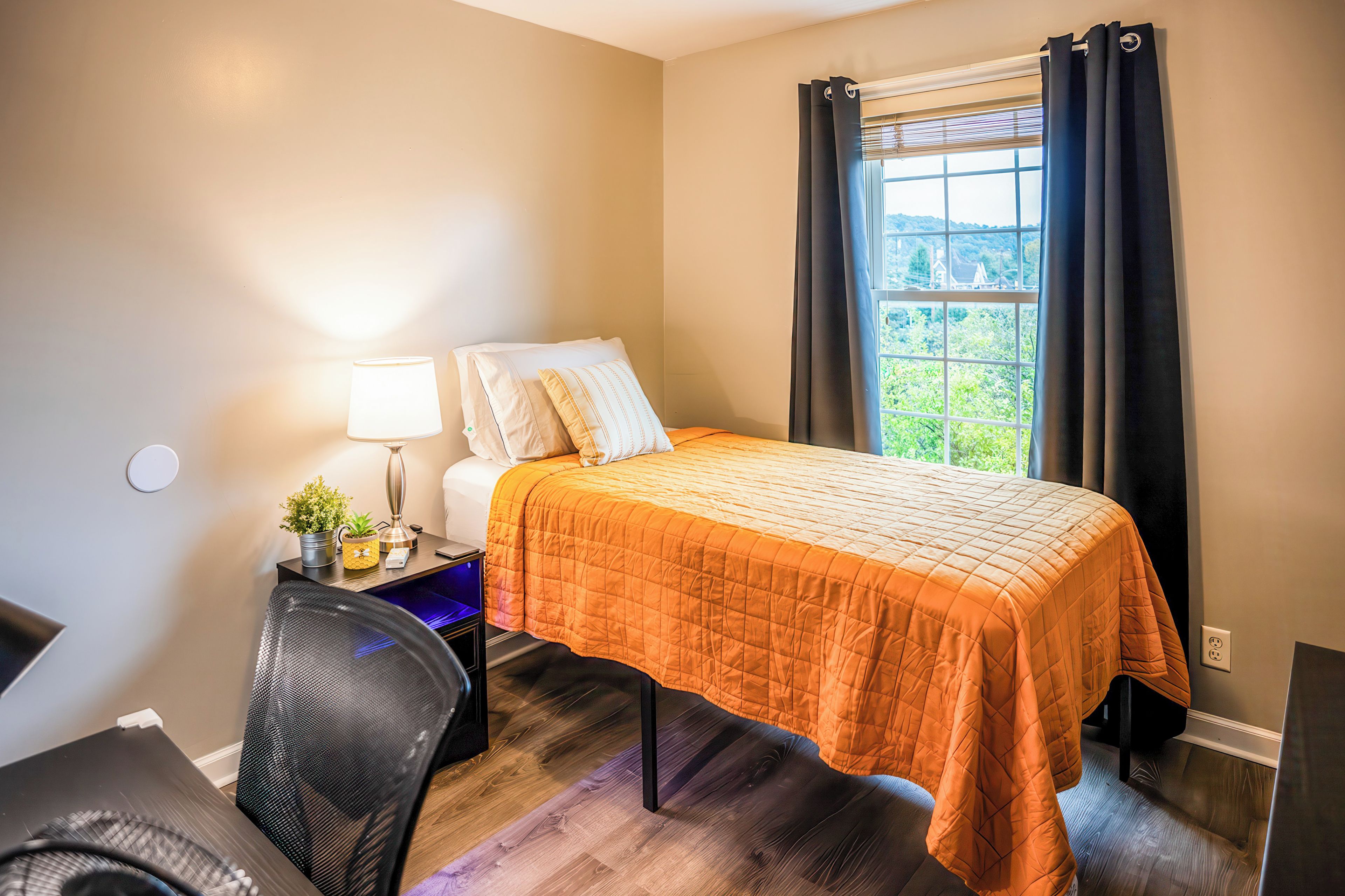 A hotel room with a bed, a desk, a chair, a lamp, and a window with curtains.