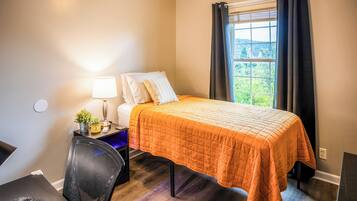 A hotel room with a bed, a desk, a chair, a lamp, and a window with curtains.
