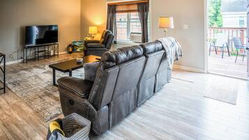 A living room with a leather sofa, a TV, a coffee table, and a dining table.