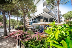 A modern hotel with a glass facade, outdoor seating, and a well-maintained garden. - Hotel Renzo (Cesenatico)