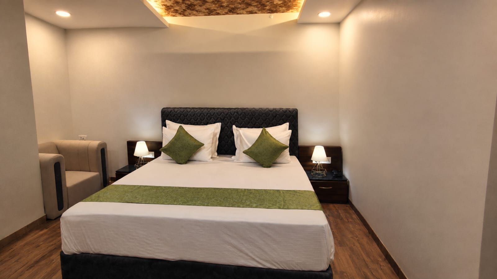 A hotel room with a large bed, two bedside tables with lamps, a chair, and a ceiling light fixture.