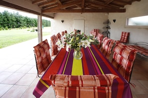 A covered outdoor dining area with a long table, striped tablecloth, and matching chairs. - Charming house in Quercy – private heated pool (15×6 m) and separate guesthouse (Roquecor)