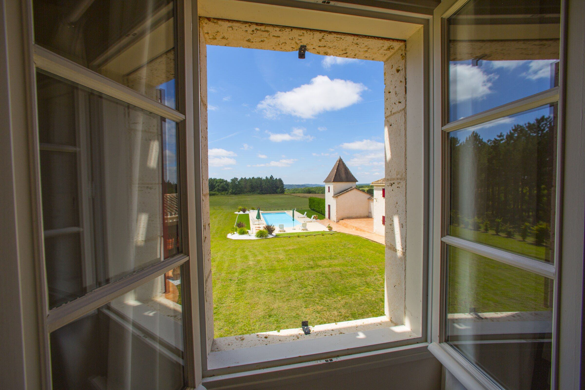 Une vue depuis une fenêtre d’une propriété dotée d’une pelouse, d’une piscine et d’un petit bâtiment avec un toit en forme de pignon.