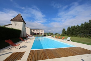 A swimming pool with lounge chairs, a wooden deck, and a large building in the background. - Charming house in Quercy – private heated pool (15×6 m) and separate guesthouse (Roquecor)