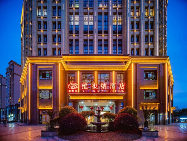 A hotel with a prominent neon sign, a fountain in the courtyard, and a modern building facade. - Vienna Hotel (Chengdu)