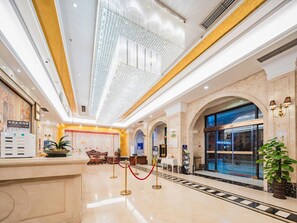 A hotel lobby with a reception desk, seating area, and a large arched window. - Vienna Hotel (Chengdu)